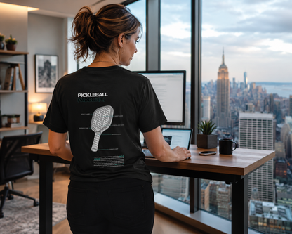 Woman wearing pickleball blueprint shirt at standing desk with Manhattan view