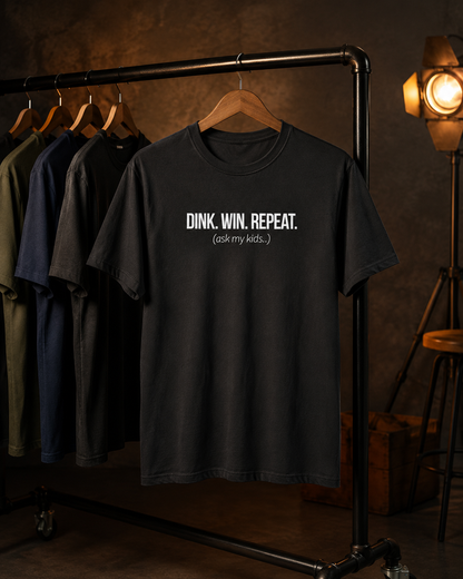 Dink Win Repeat Ask My Kids shirt on clothing rack in moody studio