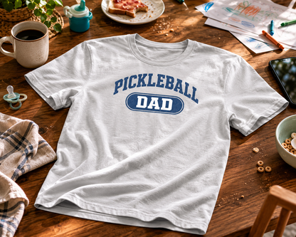 Pickleball Dad shirt laid flat on family dining table with coffee and baby pacifier