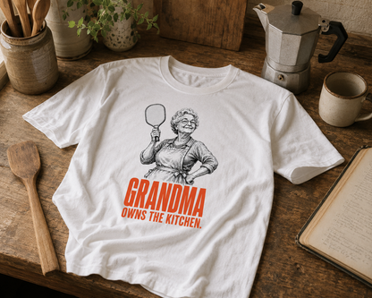 Grandma Owns the Kitchen pickleball shirt laid on rustic kitchen counter with recipe book and spatula