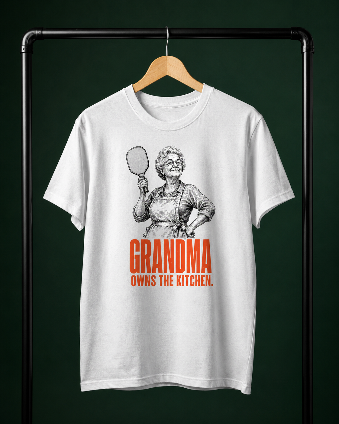 Grandma Owns the Kitchen pickleball shirt on clothing rack in bottle green editorial studio