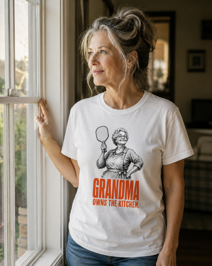 Woman wearing Grandma Owns the Kitchen pickleball shirt standing at window in natural daylight